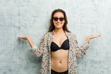 Bikini giyen genç Avrupalı kadın kollarıyla ölçeği yapıyor, mutlu ve kendinden emin hissediyor..