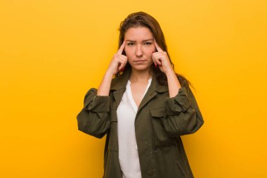 Genç Avrupalı kadın sarı arka plan üzerinde izole bir görev üzerinde duruldu, onu işaret eden başını işaret onu işaret parmakları tutmak.