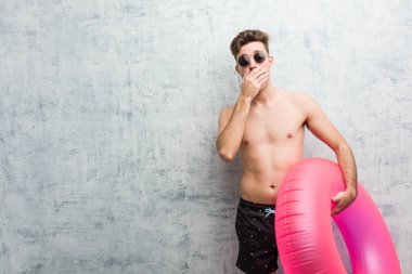 Elinde pembe şişme bir donut tutan mayo giyen genç adam ağzını elleriyle kapatırken şok oldu..