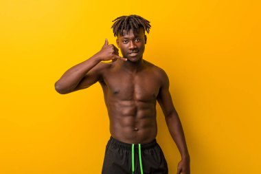 Genç siyah adam mayo giyiyor. Cep telefonu hareketini parmaklarıyla gösteriyor..