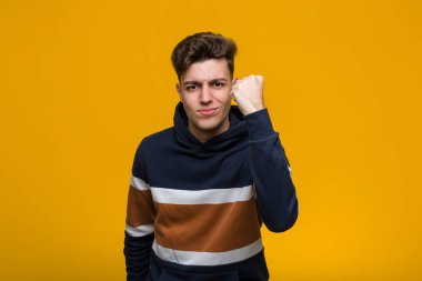 Kapüşonlu genç adam kameraya yumruğunu gösteriyor, agresif yüz ifadesi..