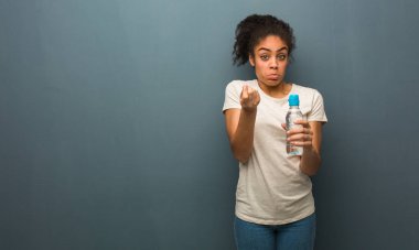 Genç siyahi kadın ihtiyaç jesti yapıyor. Elinde bir su şişesi var..