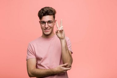 Genç havalı beyaz adam iki numarayı parmaklarıyla gösteriyor..