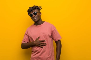 Güneş gözlüğü takan genç siyahi adam karnına dokunuyor, nazikçe gülümsüyor, yemek yiyor ve tatmin oluyor..