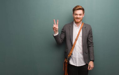 Genç kızıl saçlı iş adamı zafer jesti yaparak eğleniyor ve mutlu oluyor.