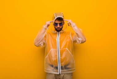 Yağmurluk giyen genç adam konsantrasyon hareketi yapıyor.