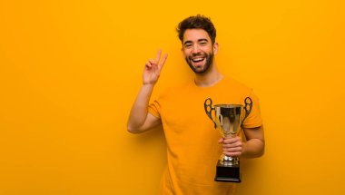 Elinde kupa tutan genç bir adam zafer jesti yapıyor.