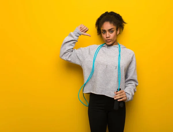 Young fitness black woman pointing fingers, example to follow. Holding a jump rope.