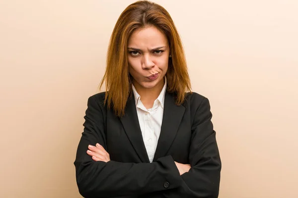 Young caucasian business woman frowning her face in displeasure, keeps arms folded.