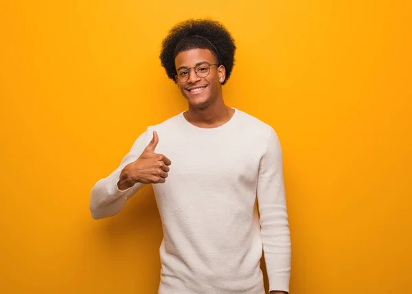 年轻的非洲裔美国人微笑着越过橙色的墙壁 竖起大拇指 — 图库照片