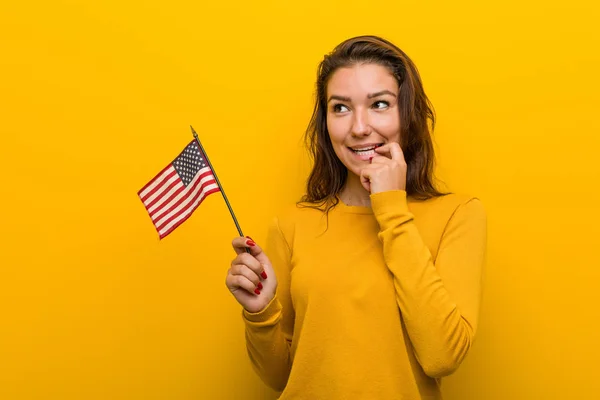 Young woman holding an united states flag relaxed thinking about something looking at a copy space.