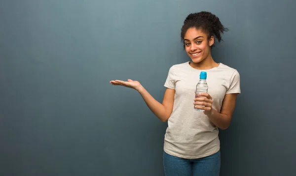 Young black woman holding something with hand. She is holding a water bottle.