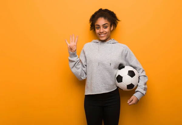 Young fitness black woman showing number four. Holding a soccer ball.