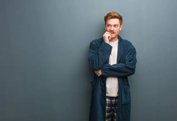 Young redhead man in pajama relaxed thinking about something looking at a copy space