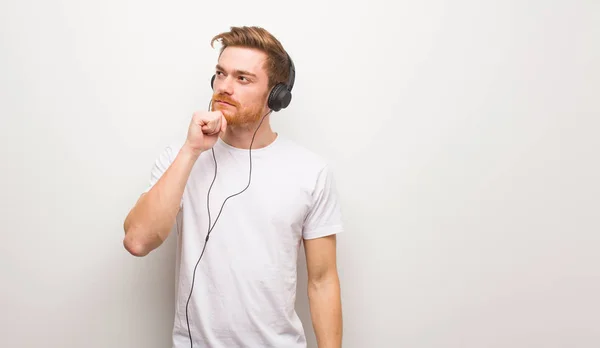 Ung Rödhårig Man Tvivlar Och Förvirrad Lyssna Musik Med Hörlurar — Stockfoto