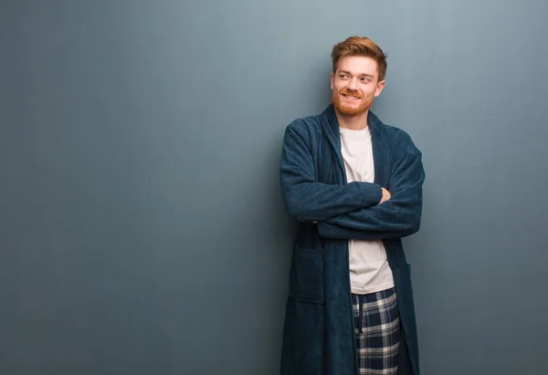Young redhead man in pajama smiling confident and crossing arms, looking up