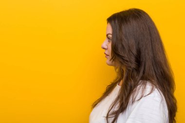 Genç, kıvrımlı, iri bir kadın sola bakıyor..