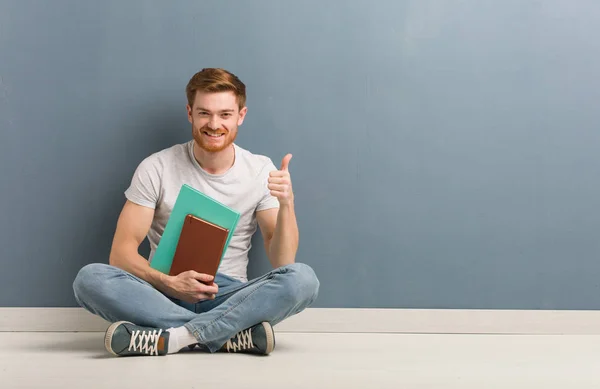 Mladý Zrzavý Student Který Sedí Podlaze Usmívá Zvedá Palec Sebe — Stock fotografie