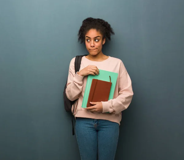 Young student black woman thinking about an idea. She is holding books.