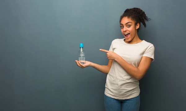 Young black woman holding something with hand. She is holding a water bottle.