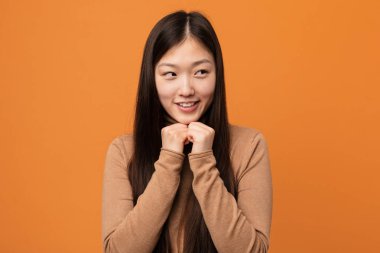 Genç, güzel Çinli kadın ellerini çenesinin altında tutuyor ve mutlu bir şekilde yan tarafa bakıyor..