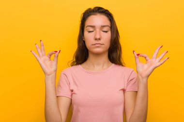 Genç Avrupalı kadın sarı arka plan üzerinde izole zor iş gününden sonra rahatlatır, o yoga yapıyor.