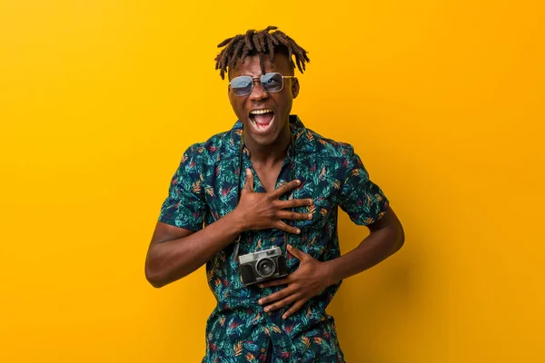 Young black rasta man wearing a vacation look laughs happily and has fun keeping hands on stomach.