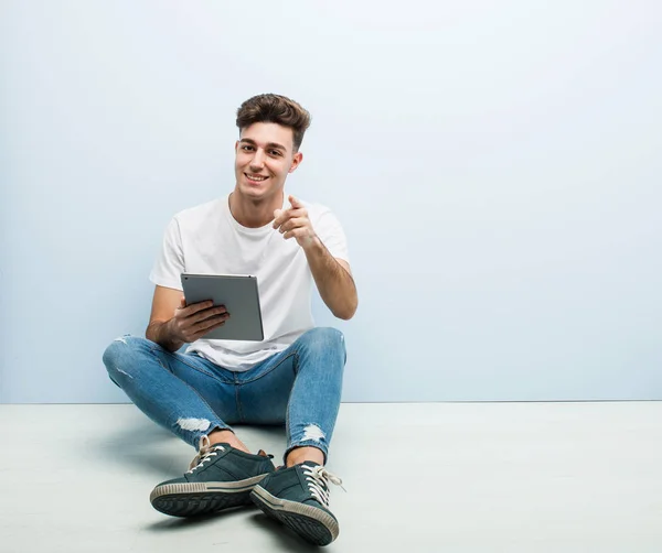 Joven Sosteniendo Una Tableta Sentada Interior Sonrisas Alegres Apuntando Hacia — Foto de Stock