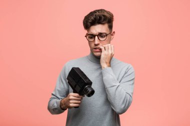 Genç entellektüel bir adam elinde kamera tutuyor tırnaklarını yiyor, gergin ve çok endişeli..