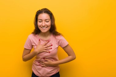 Sarı arka planda izole edilmiş genç Avrupalı kadın mutlu bir şekilde gülüyor ve ellerini karnında tutarak eğleniyor..