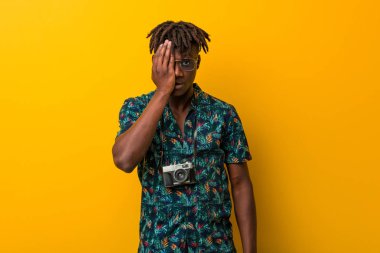 Tatil giymiş genç siyah Rasta adam yüzünün yarısını avuç içiyle örterek eğleniyor..