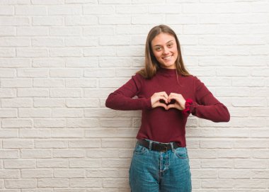 Tuğla duvarın üzerinden kalp şeklinde elleri olan genç, havalı bir kadın.