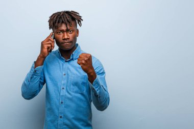 Genç Rasta siyahi adam kameraya yumruğunu gösteren bir telefon tutuyor, agresif yüz ifadesi..