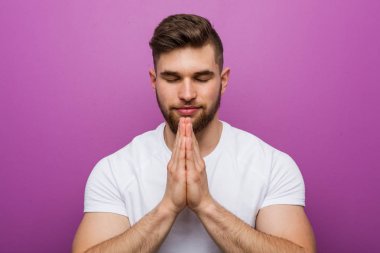 El ele tutuşup dua eden yakışıklı beyaz bir adam, kendinden emin..