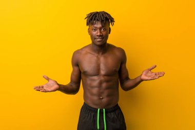 Genç siyah adam mayo giyiyor ve hoş bir yüz ifadesi sergiliyor..