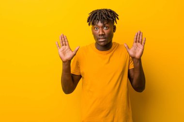 Sarı arka planda rastas giyen genç siyah bir adam tiksinti belirtisi gösteren birini reddediyor..