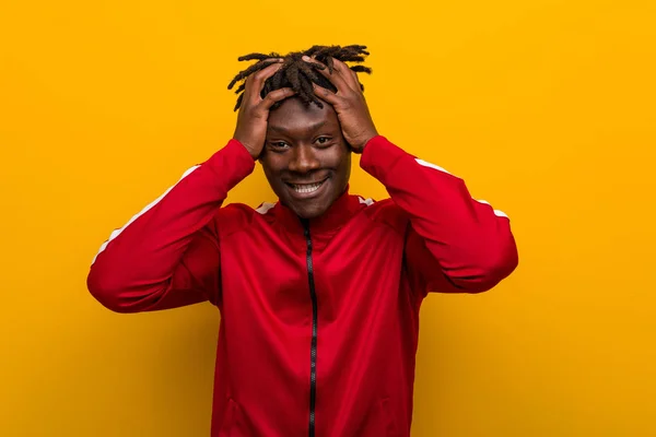 Young fitness black man laughs joyfully keeping hands on head. Happiness concept.