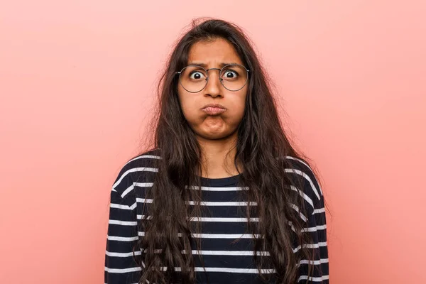 Young intellectual indian woman blows cheeks, has tired expression. Facial expression concept.