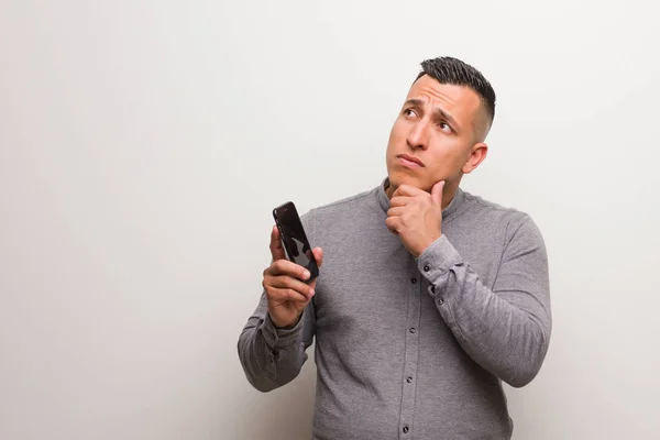 Joven Latino Sosteniendo Teléfono Dudando Confundido — Foto de Stock