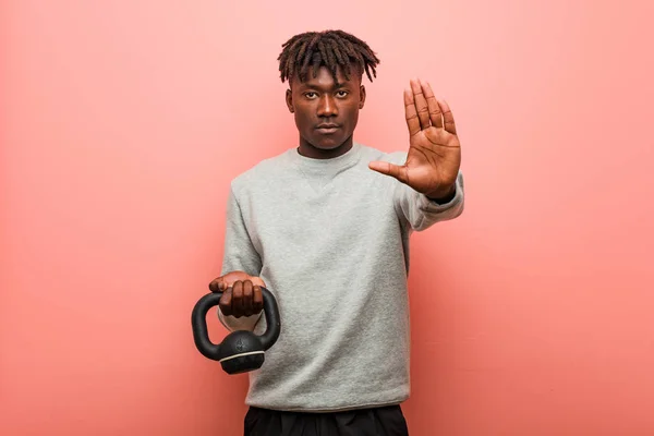 Young fitness black man holding a dumbbell standing with outstretched hand showing stop sign, preventing you.