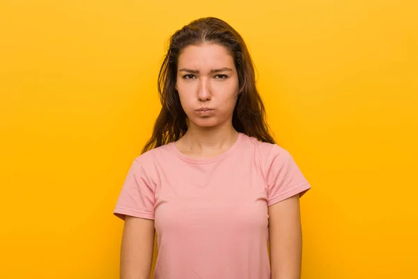 Young european woman isolated over yellow background blows cheeks, has tired expression. Facial expression concept.