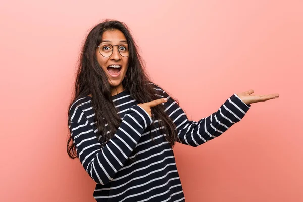 Young intellectual indian woman excited holding a copy space on palm.