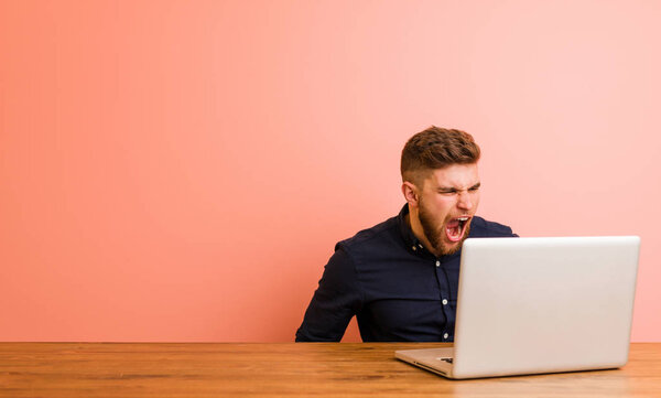 Молодой человек, работающий со своим ноутбуком, кричит в сторону копировального пространства
