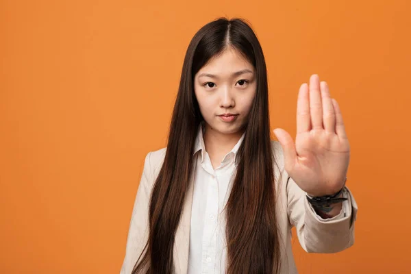 Young business chinese woman standing with outstretched hand showing stop sign, preventing you.
