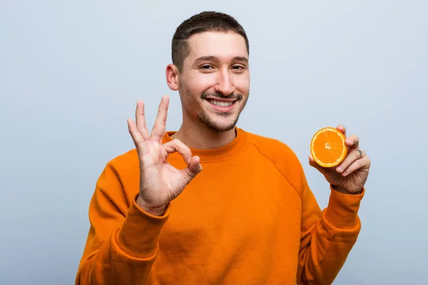Joven Hombre Caucásico Sosteniendo Una Naranja Alegre Confiado Mostrando Gesto — Foto de Stock
