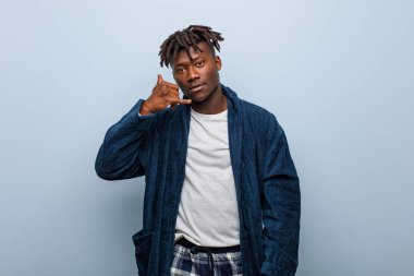 Pijama giyen Afrikalı genç bir adam cep telefonu hareketini parmaklarıyla gösteriyor..