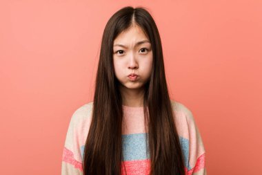 Genç havalı Çinli kadın yanaklarına üflüyor, yorgun bir ifade takınıyor. Yüz ifadesi kavramı.