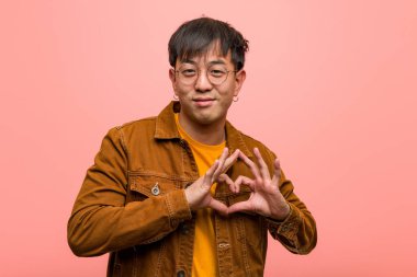 Ceket giyen genç Çinli adam elleriyle kalp şekli yapıyor.