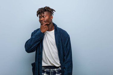 Pijama giyen Afrikalı genç bir adam şüpheli ve şüpheci bir ifadeyle yana bakıyor..
