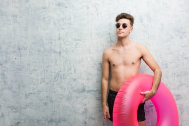 Elinde pembe şişme bir donut tutan, mayo giyen genç adam amaçları ve amaçları gerçekleştirmeyi hayal ediyor.